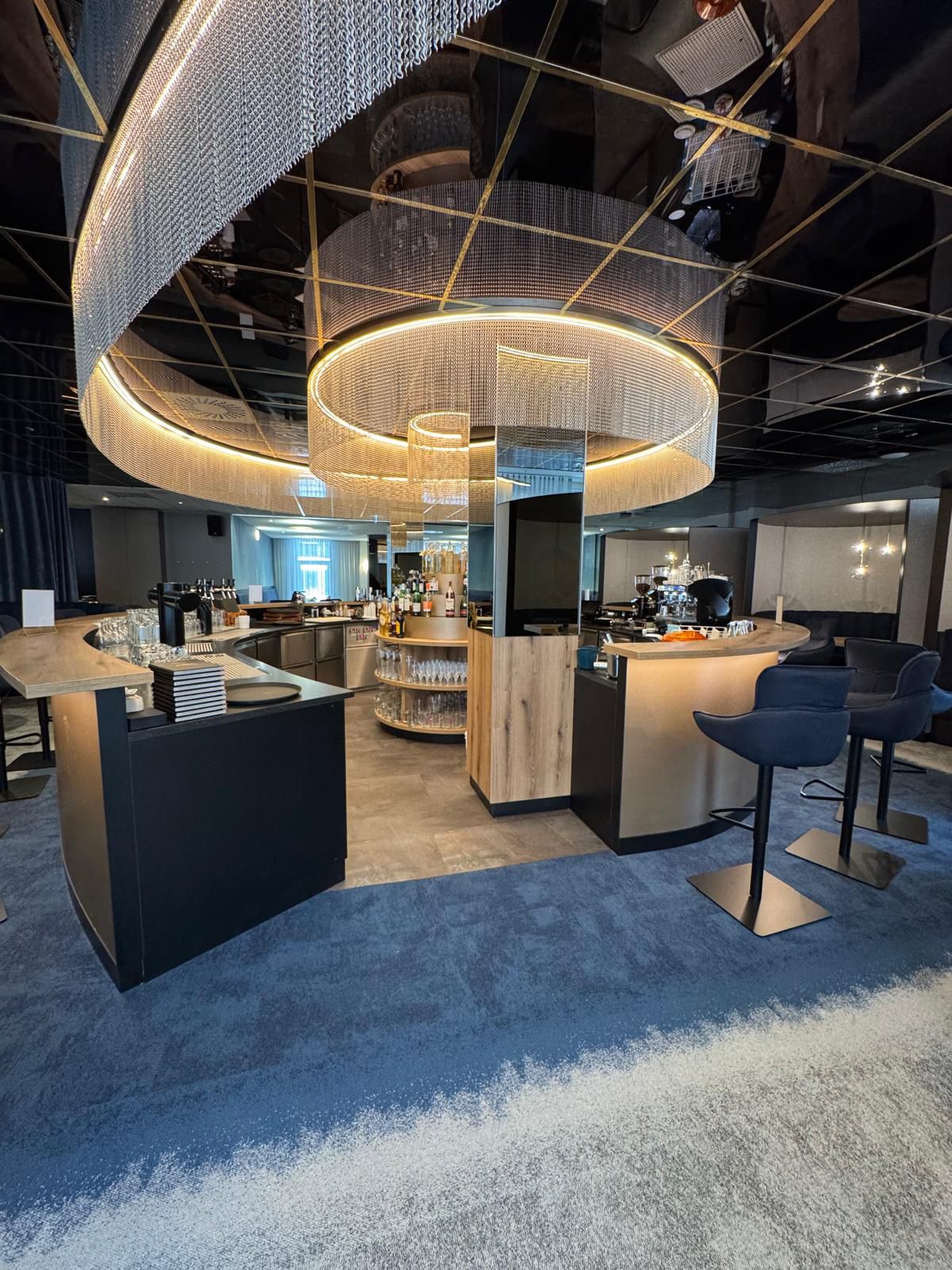 Eine moderne Bar mit runden Holzelementen, blauer Teppich und eleganter Beleuchtung
