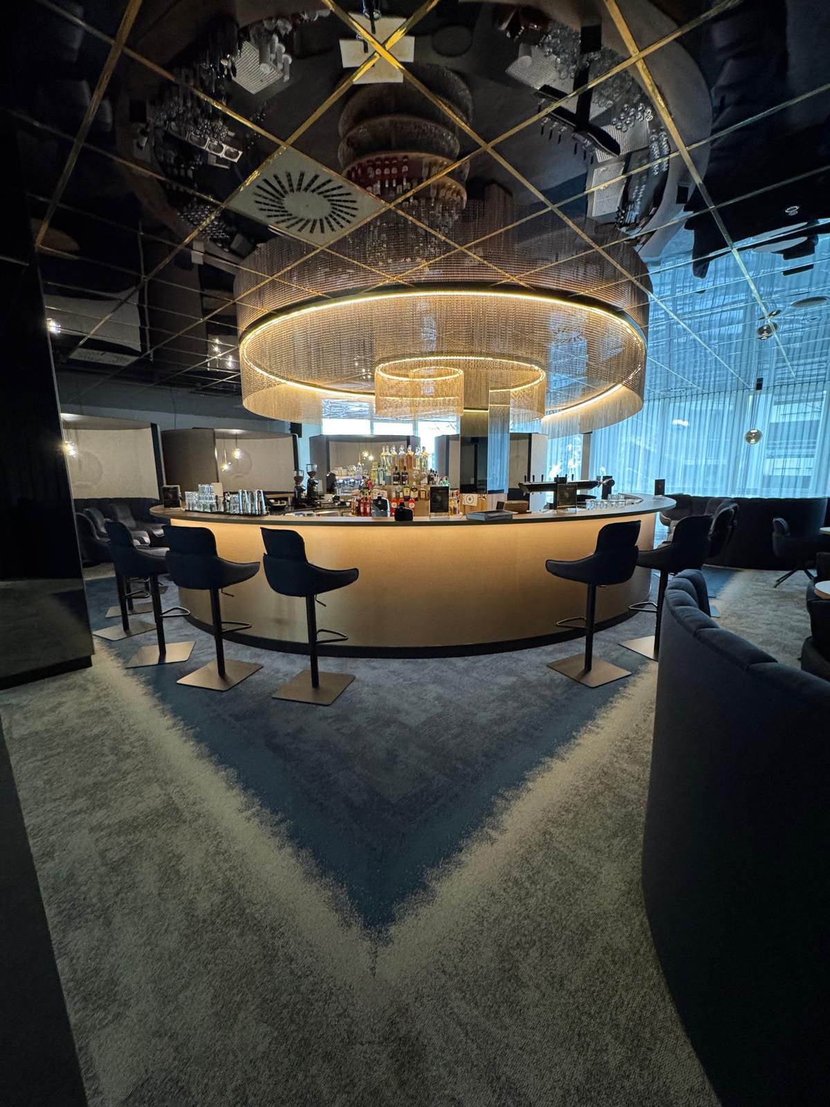 Elegante Bar mit rundem Tresen, umgeben von dunklen Barhockern und goldener Beleuchtung
