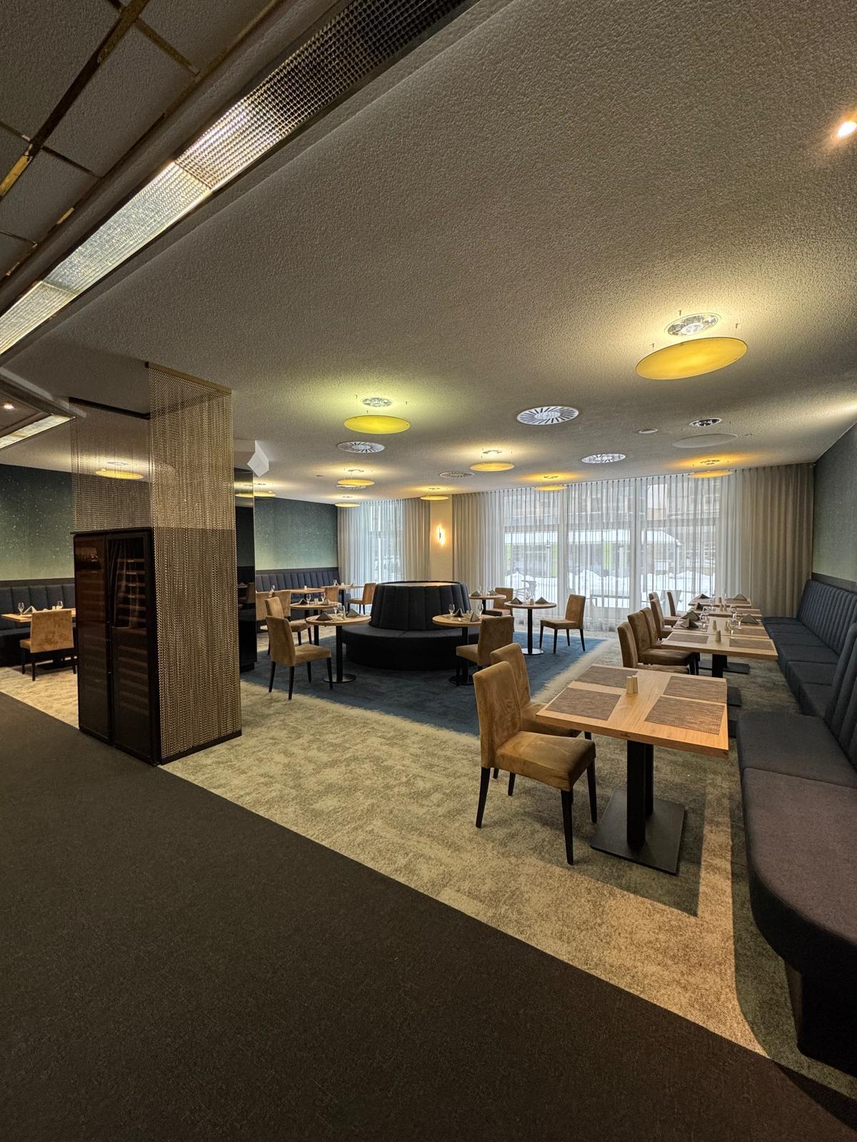 Modernes Restaurant mit beigen Stühlen, Holztischen und großen Fenstern im Hintergrund